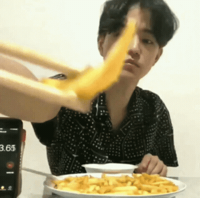 A Man Is Eating French Fries With Chopsticks And A Cell Phone In The Background . GIF