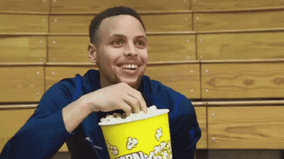 A Man Is Eating Popcorn From A Yellow Bucket That Says Corn GIF