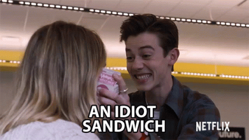 A Man Is Feeding A Woman A Sandwich That Says " An Idiot Sandwich " GIF