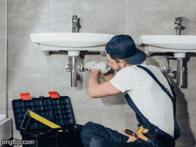 A Man Is Fixing A Sink In A Bathroom With A Toolbox Next To Him GIF