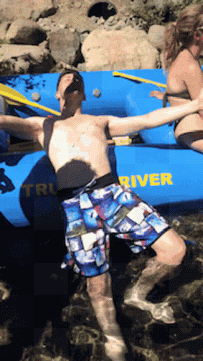 A Man Is Floating In The Water Near A Boat That Says River GIF