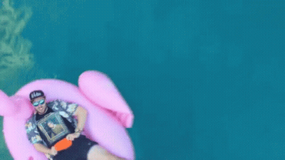 A Man Is Floating On A Pink Flamingo Float In The Water GIF