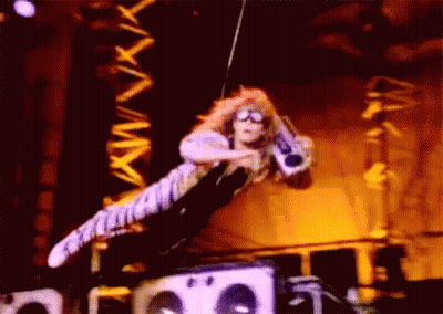 A Man Is Flying Through The Air On A Stage Holding A Microphone . GIF