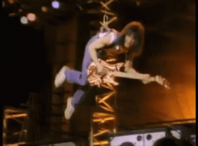 A Man Is Flying Through The Air While Holding A Guitar . GIF