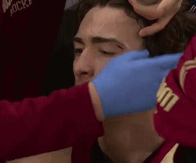 A Man Is Getting A Bandage On His Forehead While Wearing A Red Shirt That Says Hockey GIF