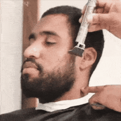 A Man Is Getting His Beard Trimmed By A Barber With A Trimmer . GIF