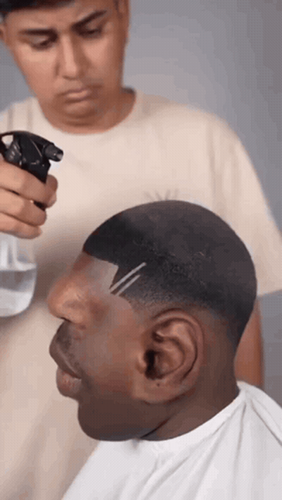A Man Is Getting His Hair Cut By A Barber While Spraying Water On His Head . GIF