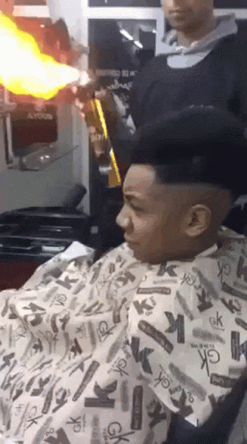 A Man Is Getting His Hair Cut By A Man Wearing A Cape That Says Ck On It GIF