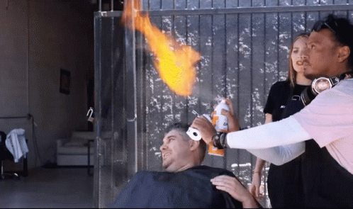 A Man Is Getting His Hair Cut By A Man Wearing Headphones And A Pink Shirt That Says Nc GIF