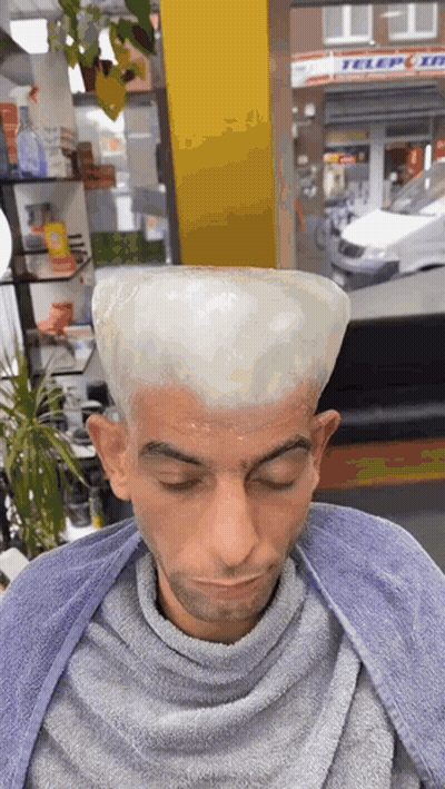 A Man Is Getting His Hair Dyed In A Barber Shop With A Sign In The Background That Says Teleport GIF