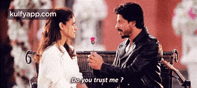 A Man Is Giving A Rose To A Woman Who Is Sitting On A Bench . GIF