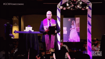 A Man Is Giving A Speech In Front Of A Picture Of A Bride And Groom And A Sign That Says Gcw GIF