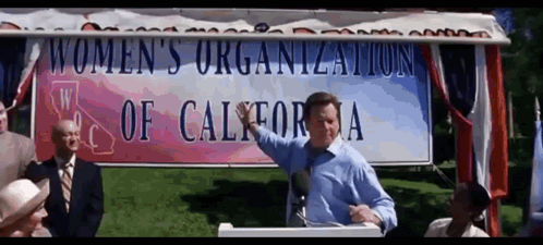 A Man Is Giving A Speech In Front Of A Women 'S Organization Of California Sign GIF