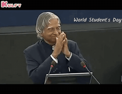 A Man Is Giving A Speech In Front Of Microphones And The Words World Student 'S Day Are On The Screen Behind Him GIF