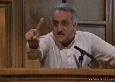 A Man Is Giving The Middle Finger While Standing In Front Of A Microphone In A Courtroom . GIF