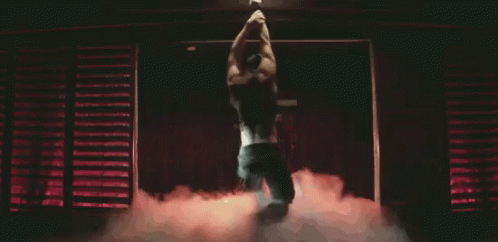 A Man Is Hanging From A Bar In A Dark Room . GIF