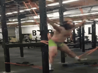 A Man Is Hanging From A Bar In A Gym While Wearing Green Underwear . GIF