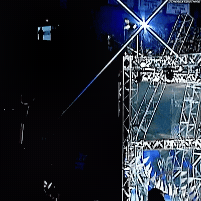 A Man Is Hanging From A Rope In A Dark Room With A Sign That Says ' Wwe ' On It . GIF