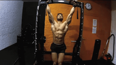 A Man Is Hanging Upside Down On A Bar In A Gym . GIF