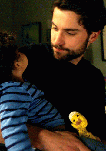 A Man Is Holding A Baby And A Stuffed Animal GIF