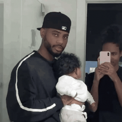 A Man Is Holding A Baby In Front Of A Mirror While A Woman Takes A Picture Of Them . GIF