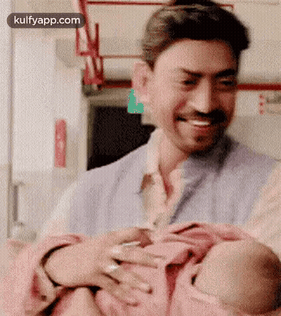 A Man Is Holding A Baby In His Arms While Smiling . GIF