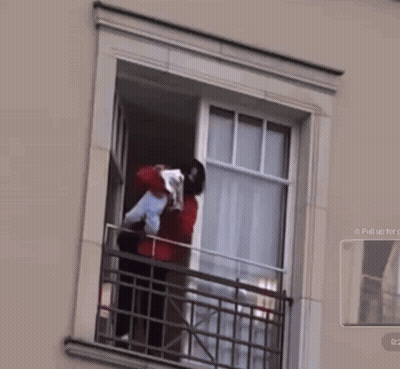 A Man Is Holding A Baby In His Arms While Standing On A Balcony GIF