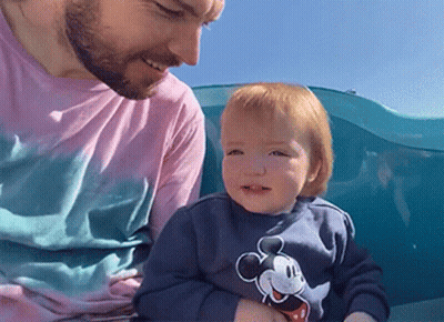 A Man Is Holding A Baby Who Is Wearing A Mickey Mouse Sweatshirt GIF