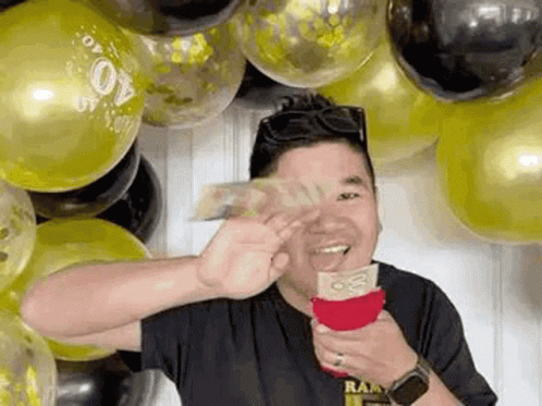 A Man Is Holding A Bag Of Money In Front Of A Bunch Of Balloons . GIF
