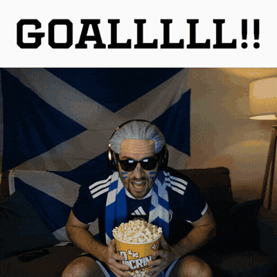 A Man Is Holding A Bag Of Popcorn With The Words Goallll !! Behind Him GIF