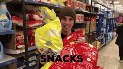 A Man Is Holding A Bag Of Snacks In A Store Aisle GIF