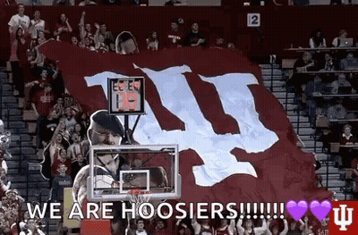 A Man Is Holding A Basketball Hoop In Front Of A Large Banner That Says We Are Hoosier ! GIF