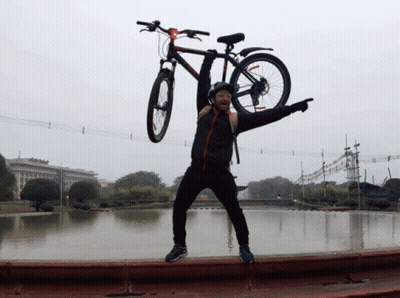 A Man Is Holding A Bicycle Over His Head And Pointing At The Camera GIF
