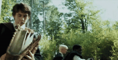 A Man Is Holding A Book In Front Of A Group Of People . GIF