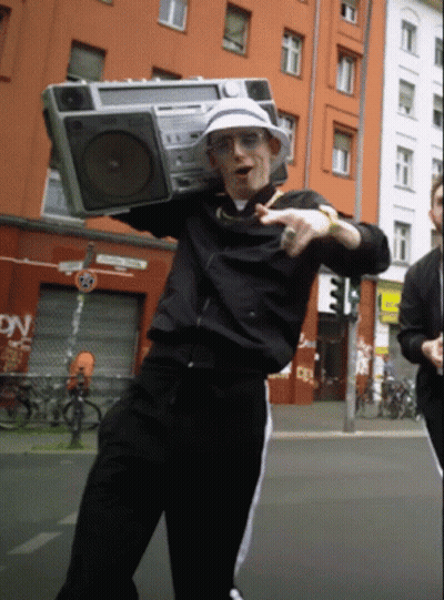 A Man Is Holding A Boombox Over His Head In Front Of A Building That Says Dn GIF