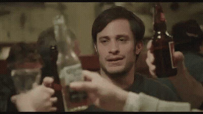 A Man Is Holding A Bottle Of Beer And A Bottle Of Tequila While A Group Of People Toast Him . GIF
