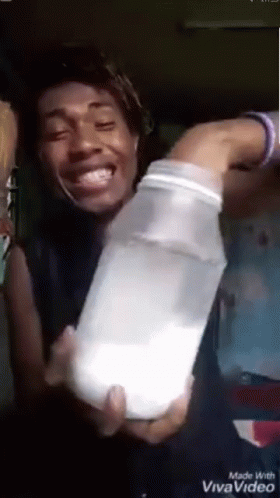A Man Is Holding A Bottle Of Milk In His Hands . GIF