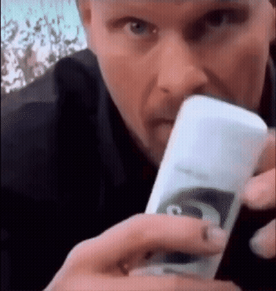 A Man Is Holding A Bottle Of Shampoo In His Hand And Drinking From It . GIF