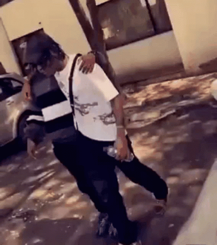 A Man Is Holding A Bottle Of Water While Dancing In The Street . GIF