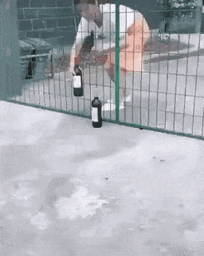 A Man Is Holding A Bottle Of Wine In Front Of A Fence GIF