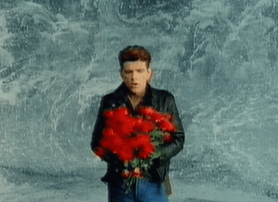 A Man Is Holding A Bouquet Of Red Flowers In His Hands . GIF