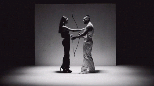 A Man Is Holding A Bow And Arrow While A Woman Holds A Bow And Arrow GIF