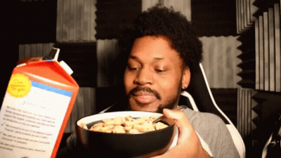 A Man Is Holding A Bowl Of Cereal In Front Of A Carton Of Cereal GIF