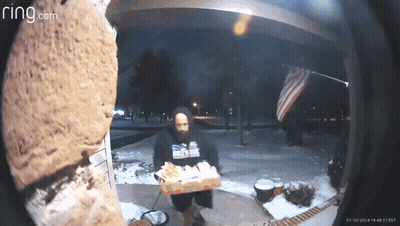 A Man Is Holding A Box Of Pizza In Front Of A Ring Doorbell . GIF