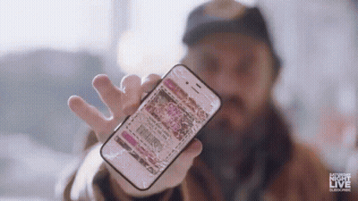 A Man Is Holding A Broken Cell Phone In His Hand And It Says Saturday Night Live On The Bottom . GIF