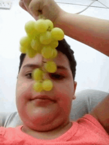 A Man Is Holding A Bunch Of Grapes Over His Face . GIF