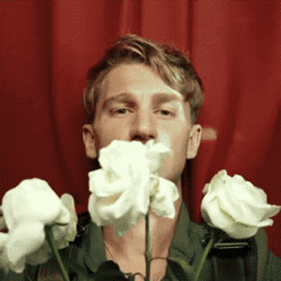 A Man Is Holding A Bunch Of White Roses In Front Of His Mouth GIF