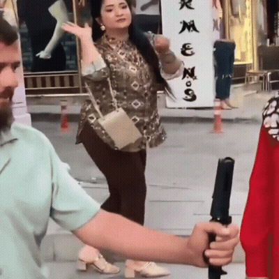 A Man Is Holding A Camera While A Woman Stands In Front Of A Sign That Says ' N ' On It GIF