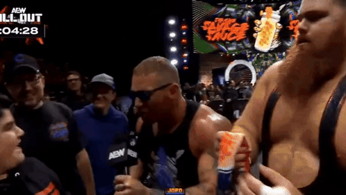 A Man Is Holding A Can Of Red Bull In Front Of A Crowd At A Wrestling Event . GIF