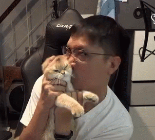 A Man Is Holding A Cat In Front Of A Black Dxr Gaming Chair GIF
